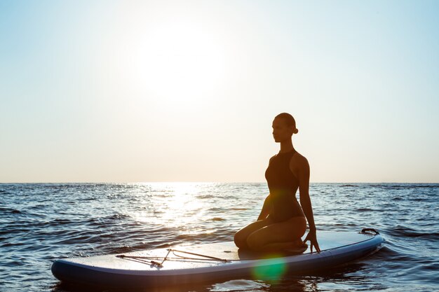 Silueta de una bella mujer practicando yoga sobre una tabla de surf al amanecer 176420 2034